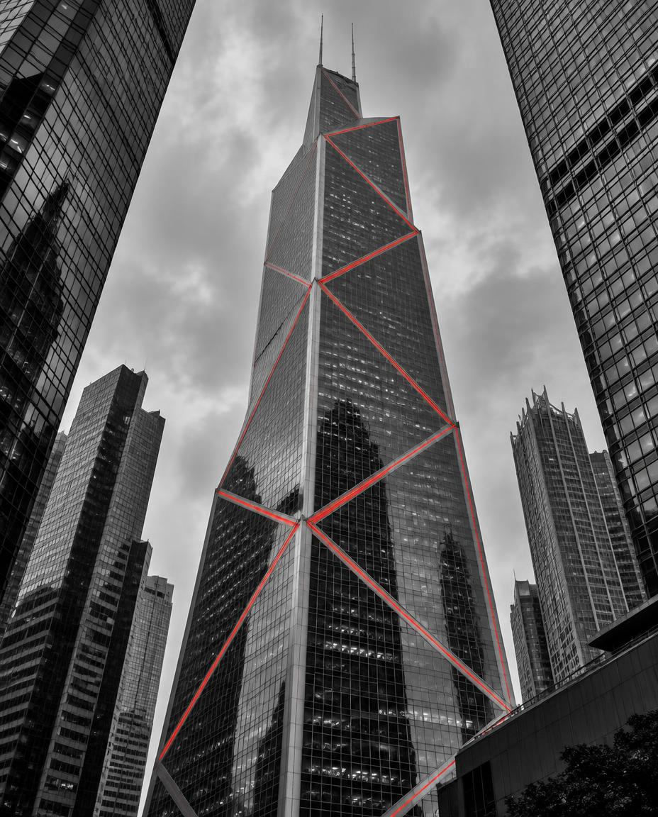 Hong Kong's Bank of China Tower seen from street level in monochrome, its diagonal bracing picked out in red